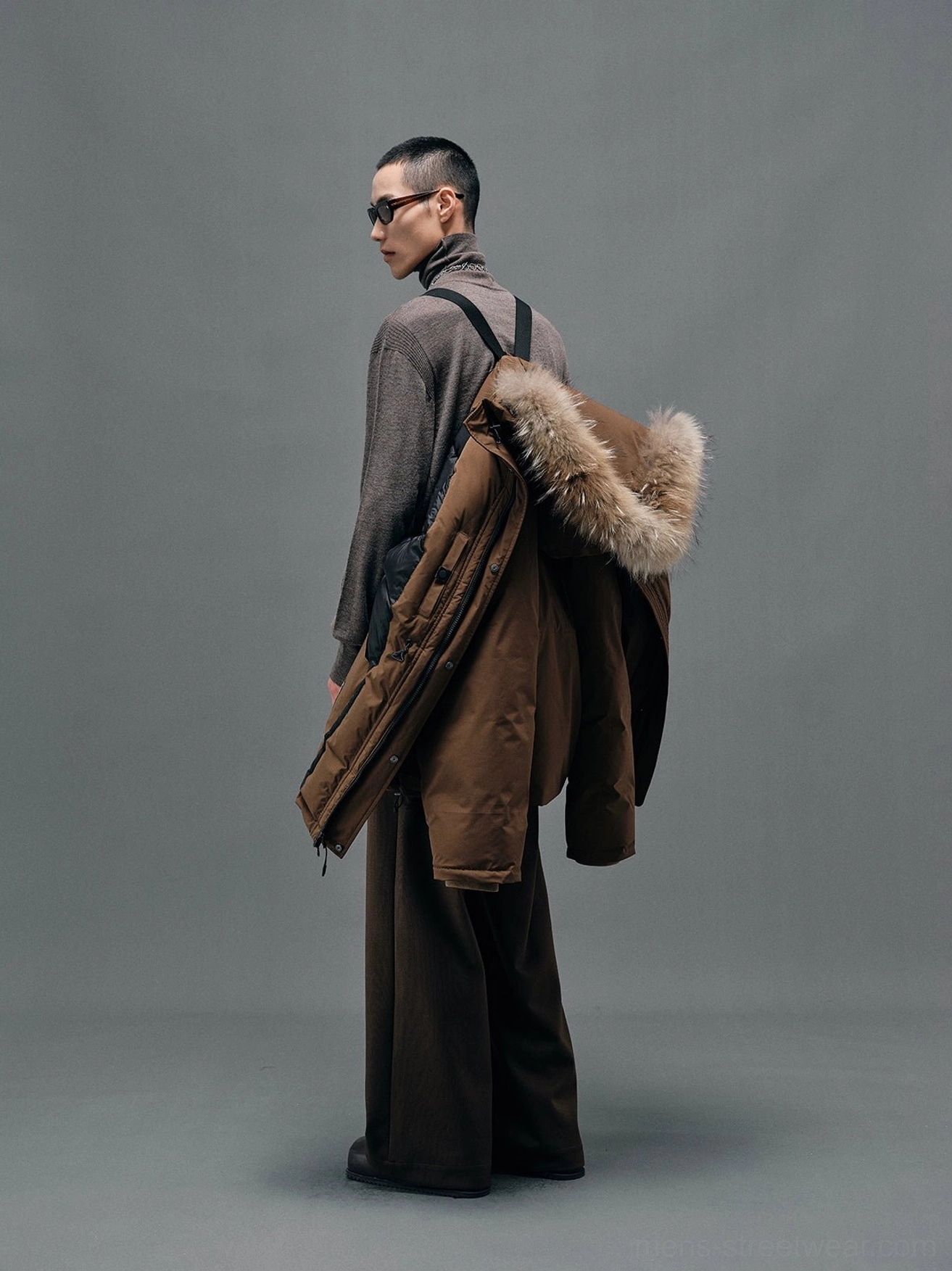 Brown fur-collar winter down coat carried over the shoulder showing the relaxed back silhouette and plush hood trim