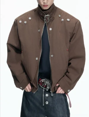 Brown high neck hardware canvas jacket worn by male model with silver buckle collar, metal rivets, and cropped streetwear fit