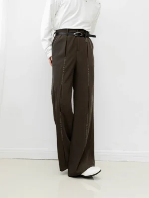 Brown high-waisted wide-leg streetwear trousers shown from the rear three-quarter angle with vertical leg stitch detailing, a black belt, white top, and white loafers
