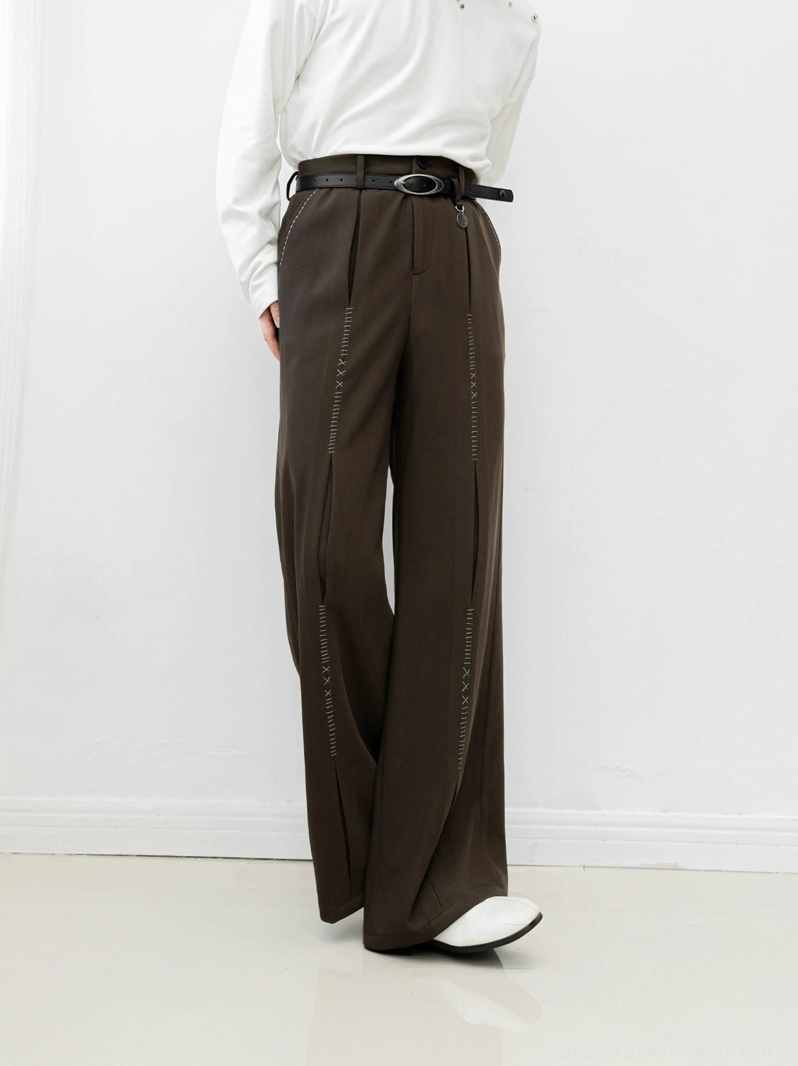 Brown high-waisted wide-leg streetwear trousers shown from the rear three-quarter angle with vertical leg stitch detailing, a black belt, white top, and white loafers