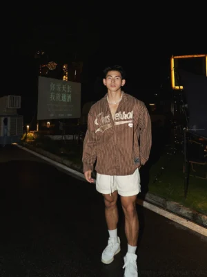 Brown oversized pinstripe baseball shirt styled with white shorts and sneakers, showing relaxed Korean streetwear proportions and an embroidered baseball-inspired front design