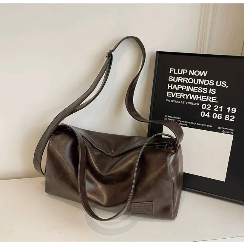 Brown PU leather streetwear sling bag with wide shoulder strap and natural folds displayed on a minimalist tabletop