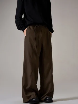Three-quarter rear view of brown wide leg trousers showing relaxed drape, pleats, hidden side pockets, and minimalist styling