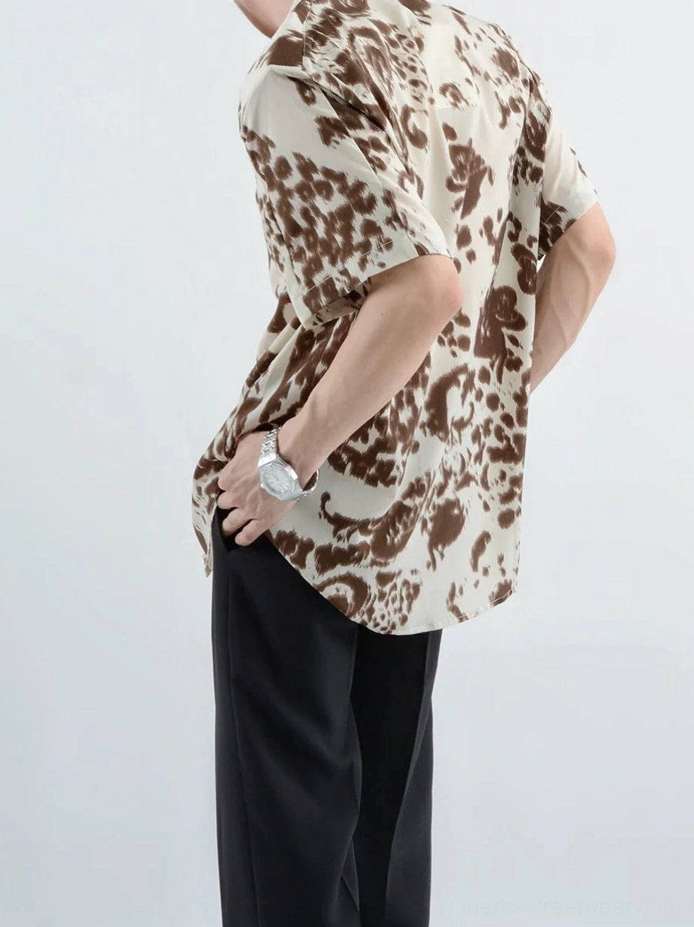 Back three-quarter view showing the loose silhouette and brown abstract retro print on an off-white short-sleeve streetwear shirt