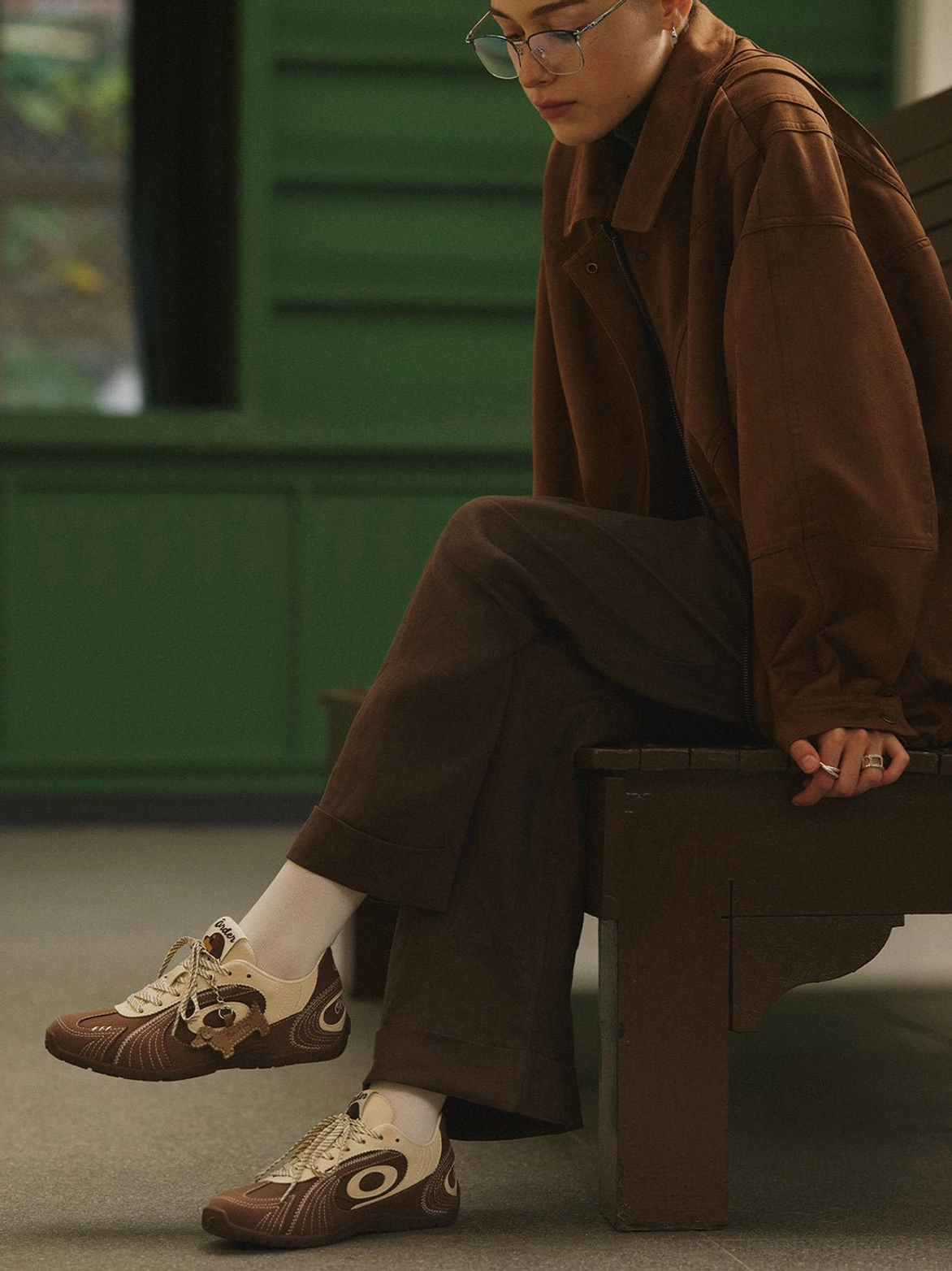 Side profile of brown retro trainers with cream swirl panels styled with corduroy jacket and wide-leg trousers