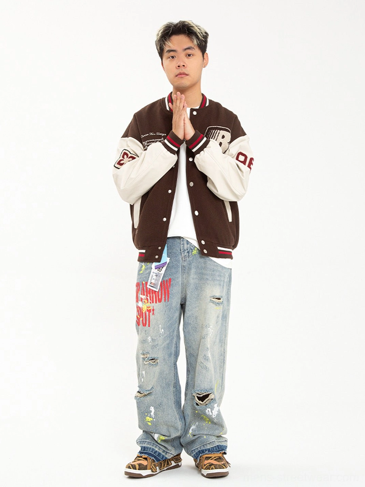 Male model styling brown camouflage rivet platform skate sneakers with a retro varsity jacket and ripped light blue jeans