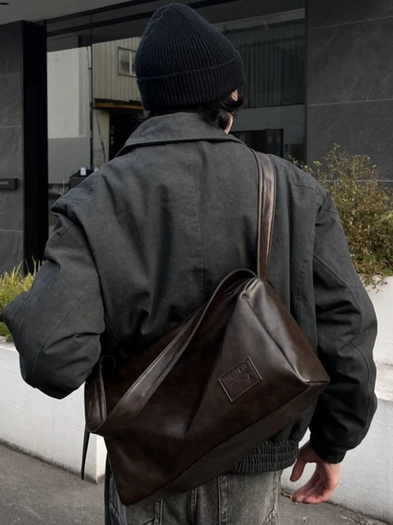Brown slouchy PU leather commuter crossbody bag resting against the back with a dark gray streetwear jacket