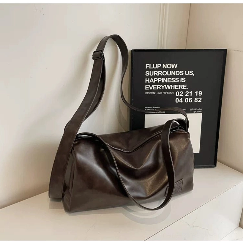 Side view of a brown soft crossbody sling bag with relaxed drape and smooth PU leather finish on a white display table