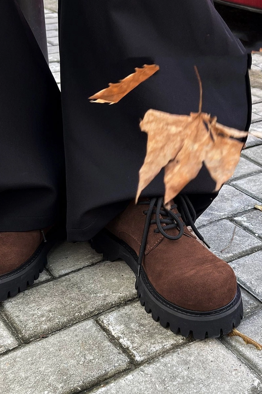 Low front street view of brown suede derby shoes with black wide-leg pants and autumn maple leaves