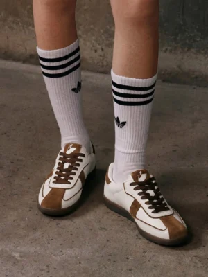 Brown suede panel gum sole sneakers worn with striped crew socks on concrete ground in a casual retro streetwear outfit