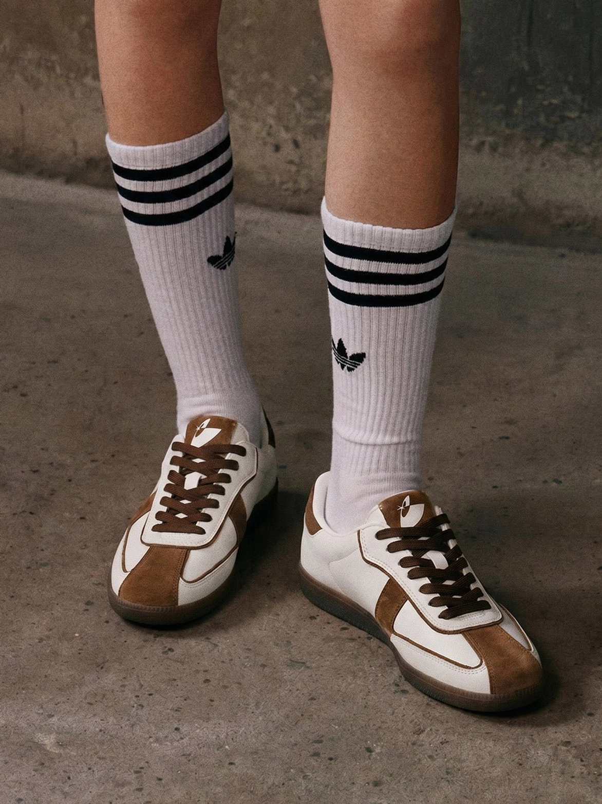 Brown suede panel gum sole sneakers worn with striped crew socks on concrete ground in a casual retro streetwear outfit