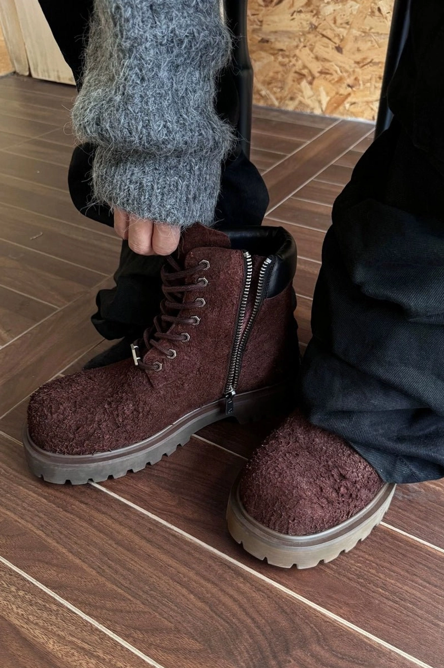 Dark brown suede lug-sole combat boots styled with baggy black pants and a fuzzy gray knit sweater indoors