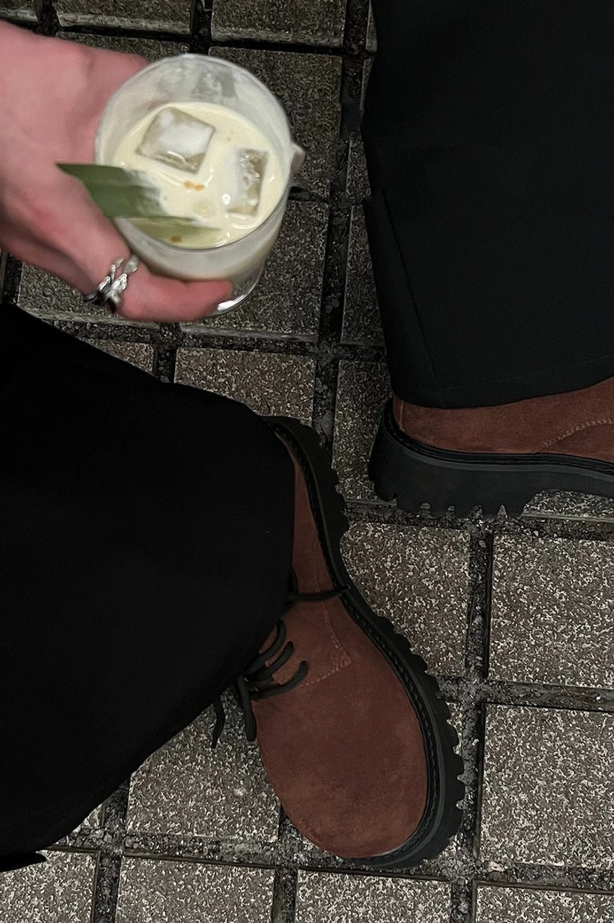 Brown suede lug-sole derby shoes worn with black wide-leg trousers in an urban streetwear outfit
