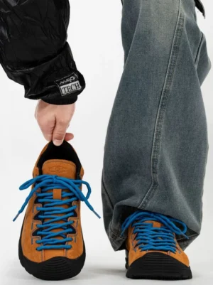 Brown suede retro trail sneakers with bright blue hiking laces and black rubber toe protection worn with loose denim jeans
