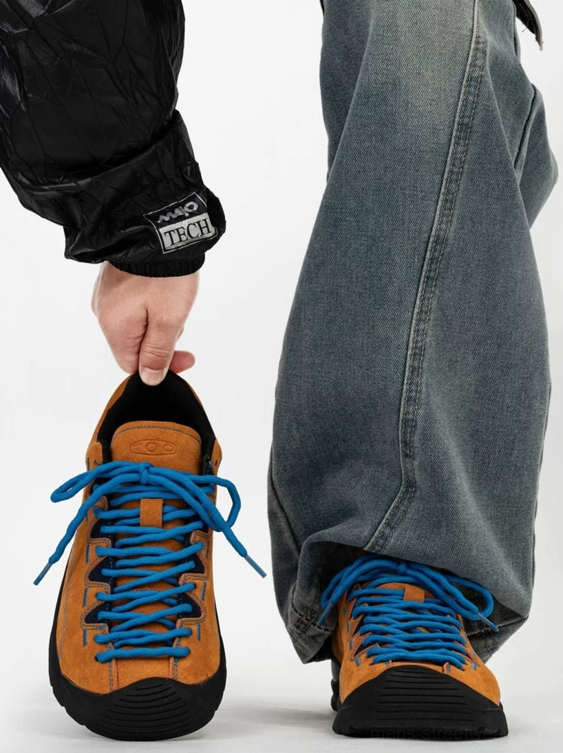 Brown suede retro trail sneakers with bright blue hiking laces and black rubber toe protection worn with loose denim jeans