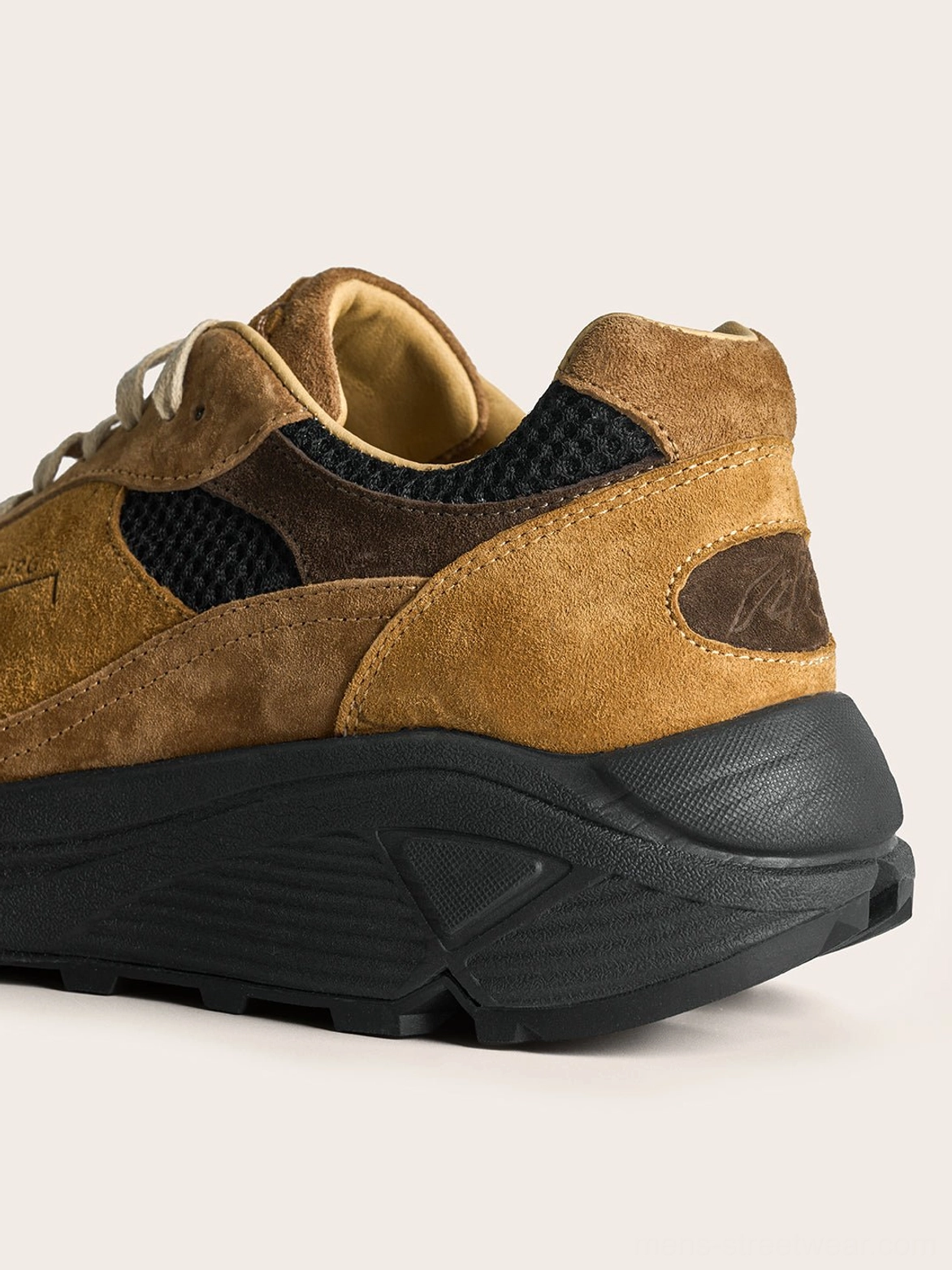 Rear side view of brown suede trail runner sneaker with embossed heel detail and curved chunky black rubber sole