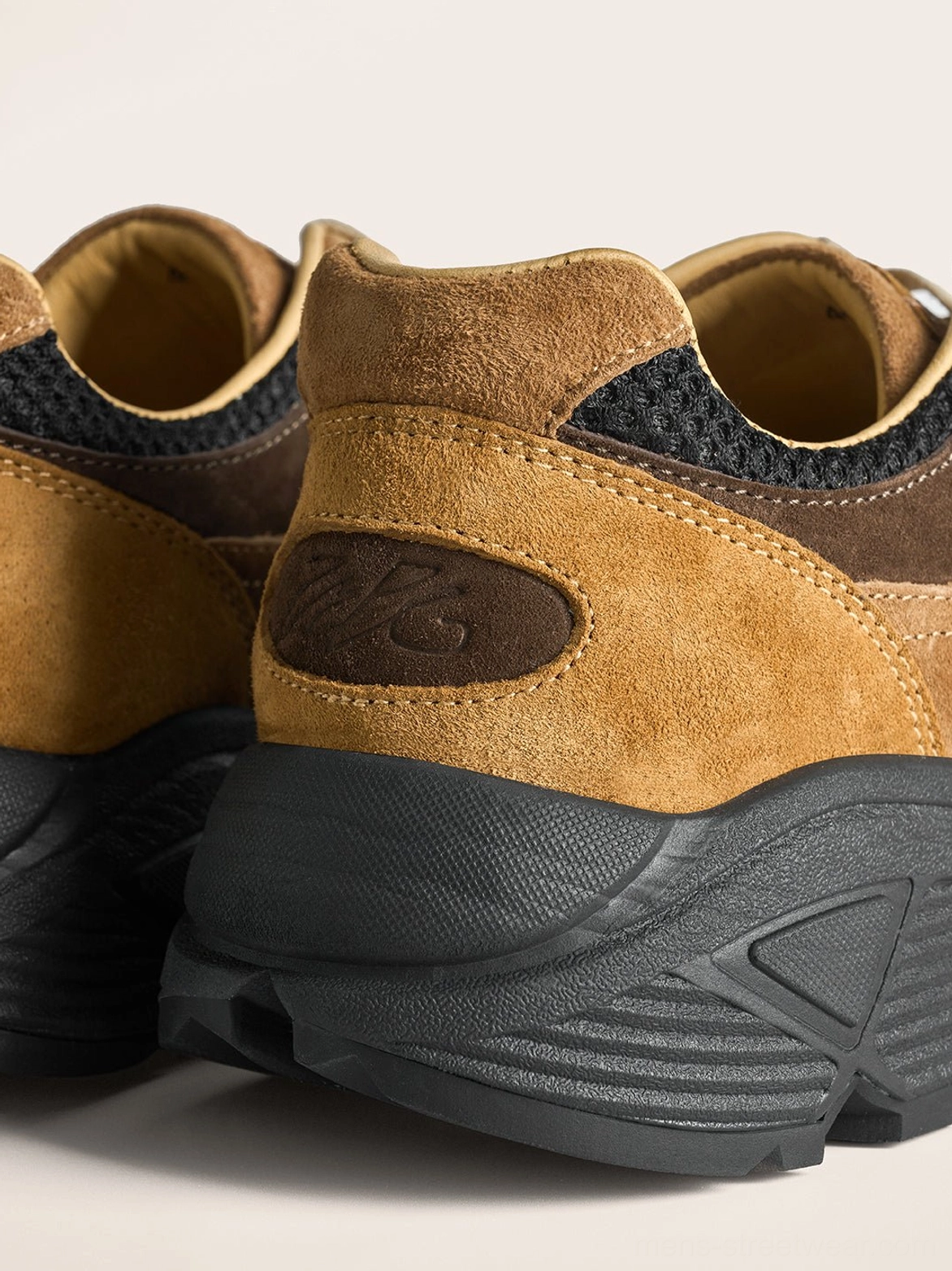 Rear three-quarter view of brown suede trail runner sneakers with padded collar embossed heel detail and chunky outsole