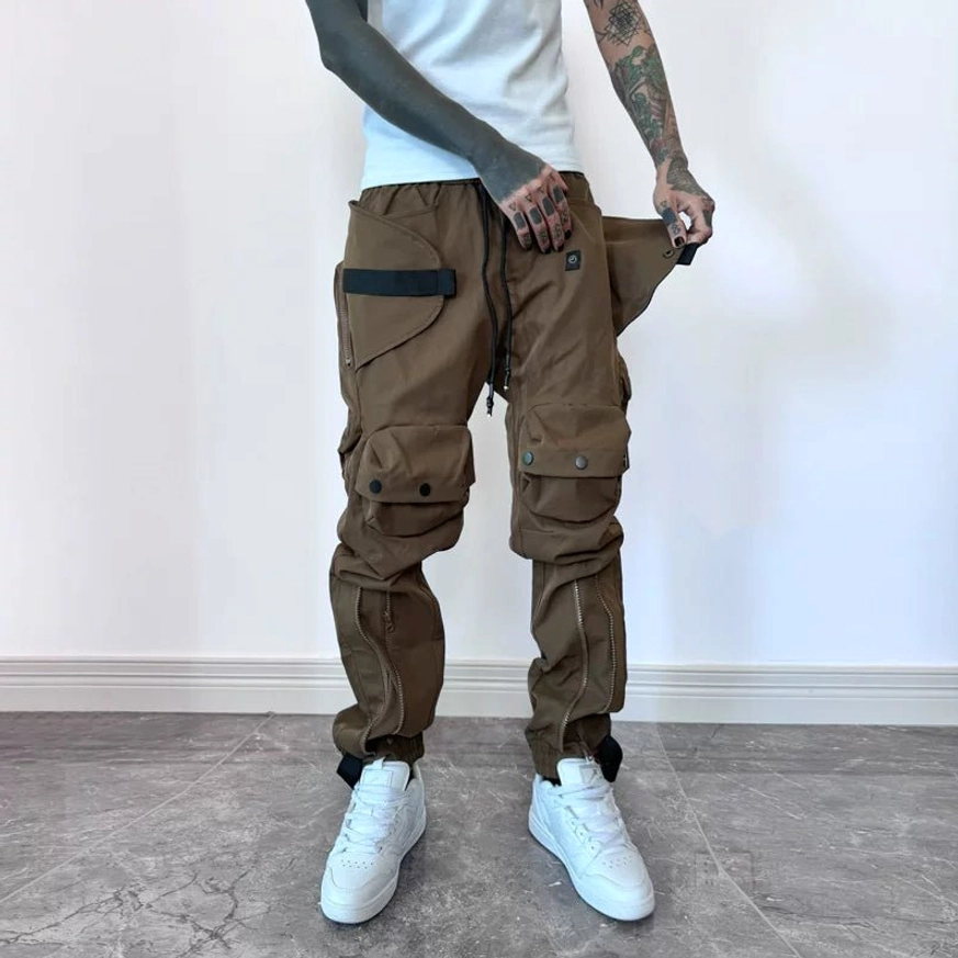 Brown techwear cargo joggers close-up showing open side cargo pocket, webbing strap details and adjustable cuff