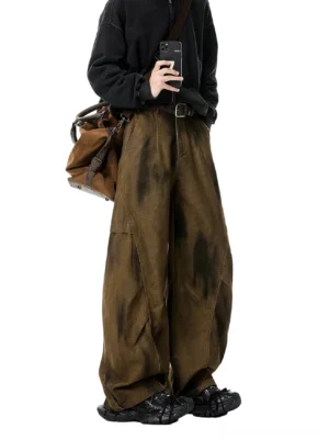 Brown weathered tie-dye wide-leg streetwear trousers shown from the side with loose draping, belt loops, chunky black sneakers, and a vintage brown crossbody bag