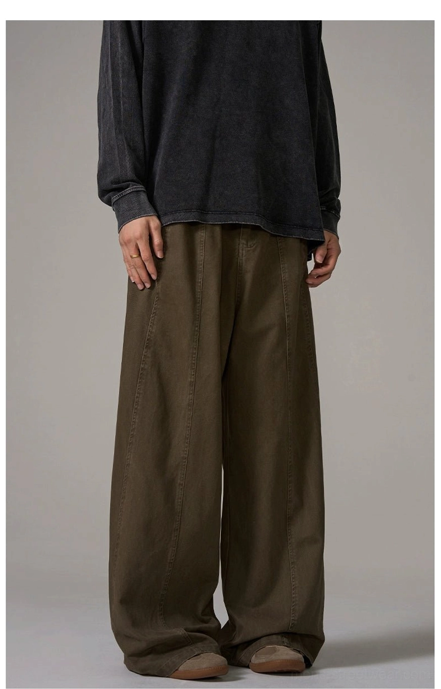 Side partial front view of brown wide-leg cotton trousers showing central seam, loose leg shape, and minimalist streetwear styling