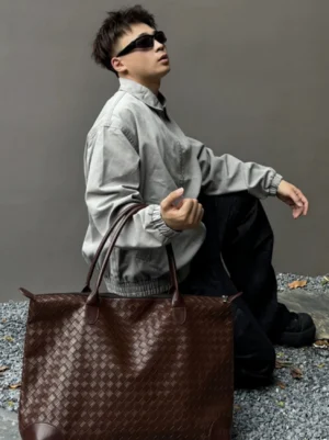 Brown woven PU leather weekender tote bag for men carried by model in outdoor streetwear outfit