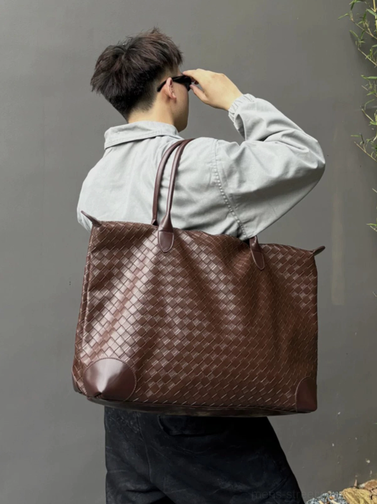 Brown woven PU leather men’s weekender tote bag worn over the shoulder from back view