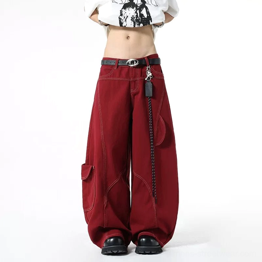 Low-angle front view of burgundy baggy cargo jeans with pooled wide-leg hem, contrast stitching, chain leather tag, belt, and chunky black shoes