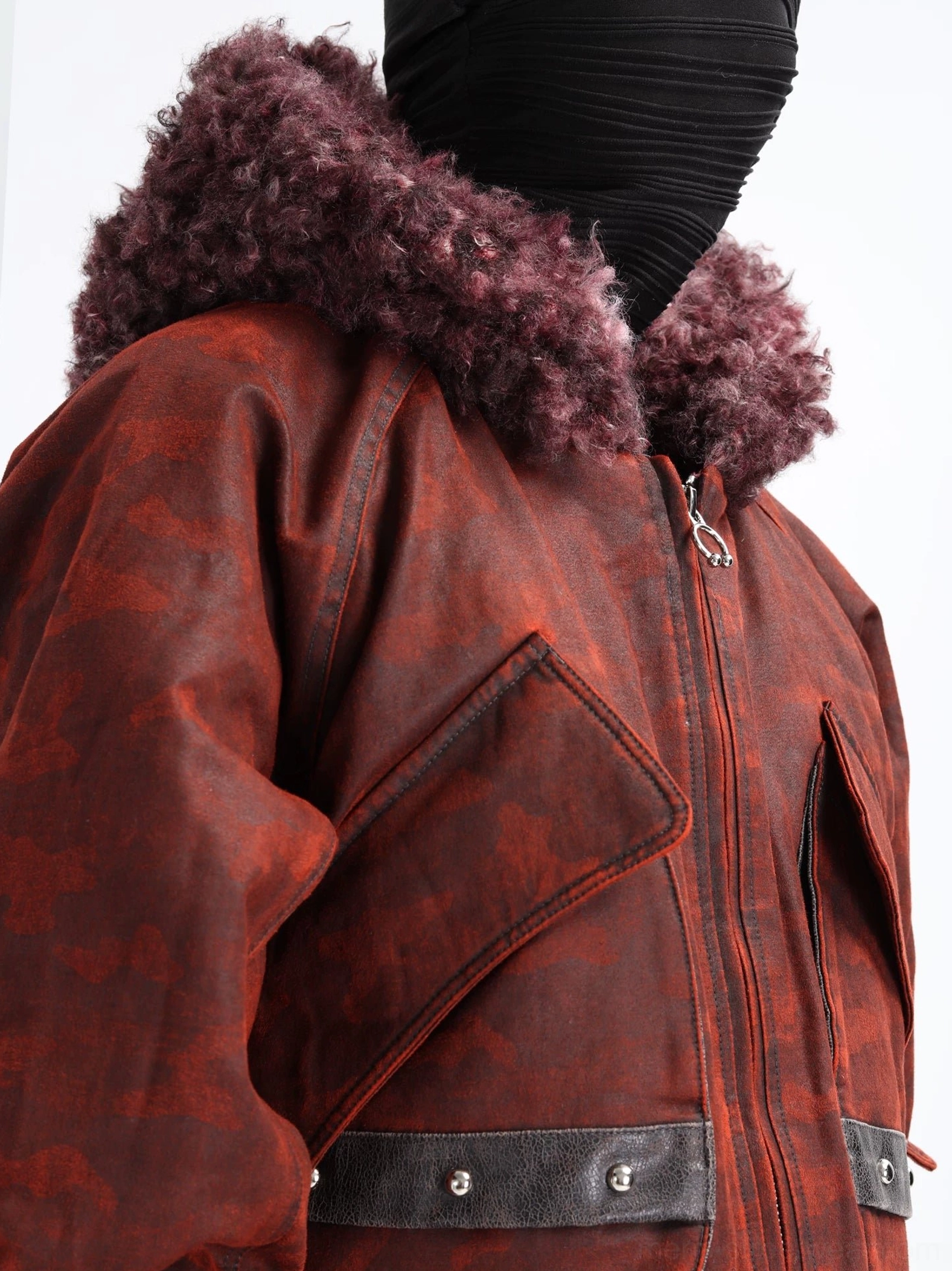 Close-up detail of burgundy faux shearling hood, distressed dark red camo fabric, polished metal zipper, and studded leather-look pocket strap on a cropped bomber jacket