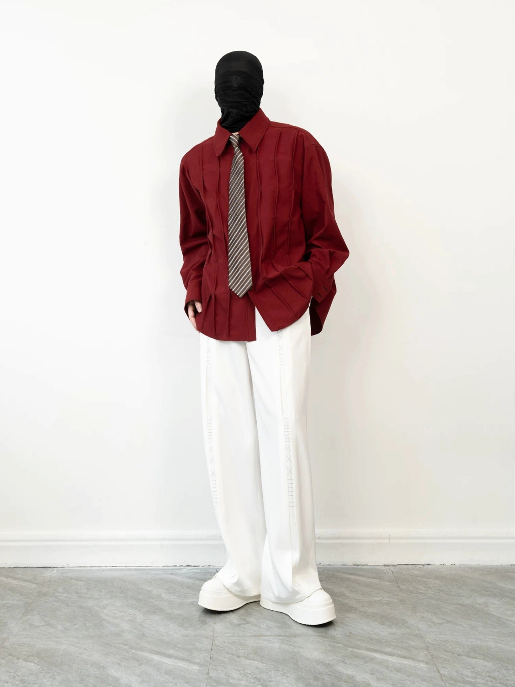 Side profile of a burgundy long sleeve pleated shirt with loose drop shoulder fit styled for modern streetwear