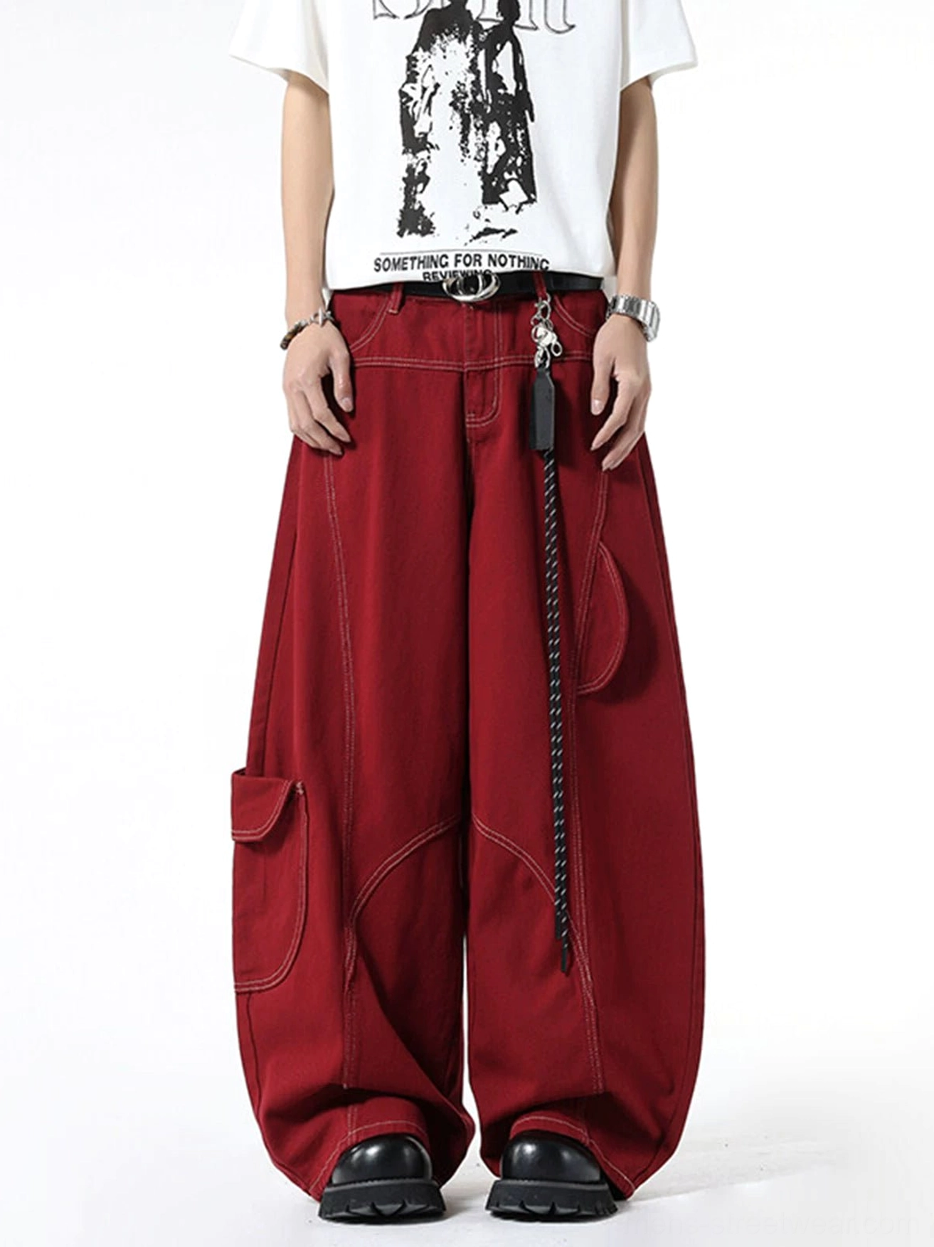 Front styling view of burgundy oversized cargo jeans with dual side utility pockets, exposed waistband, chain leather accessory, belt, and chunky footwear