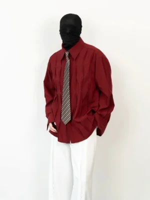 Side angle view of a relaxed burgundy pleated shirt showing the draped boxy silhouette and dimensional vertical folds