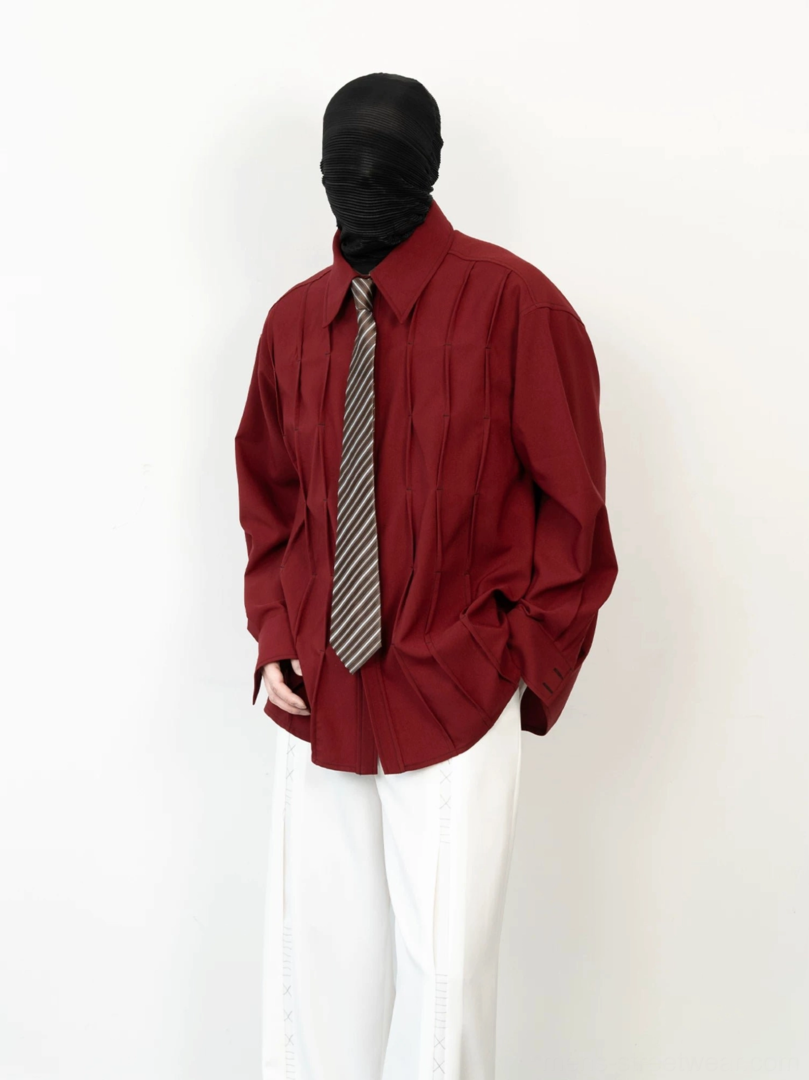 Side angle view of a relaxed burgundy pleated shirt showing the draped boxy silhouette and dimensional vertical folds