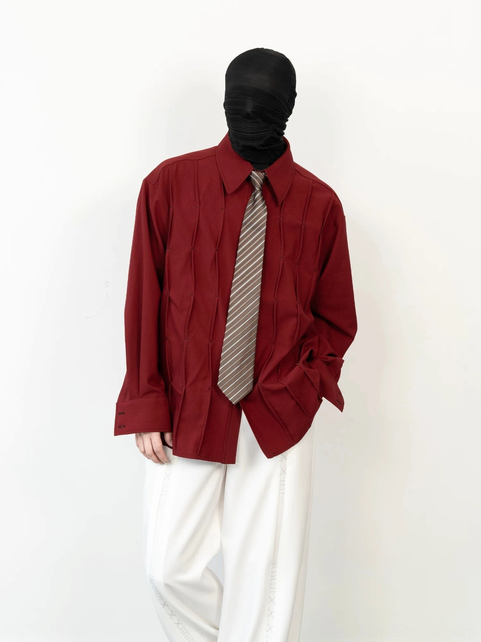 Front view of a burgundy pleated streetwear shirt with pointed collar and taupe gray striped tie styled with white wide leg pants
