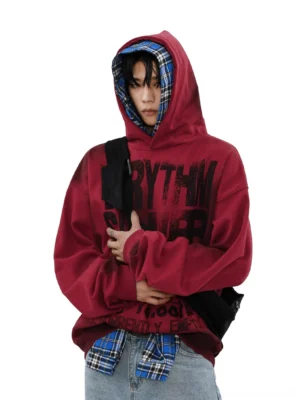 Three-quarter view of burgundy red oversized Korean streetwear hoodie with distressed rhythm lettering, blue plaid inner hood, drop shoulders, and relaxed fit