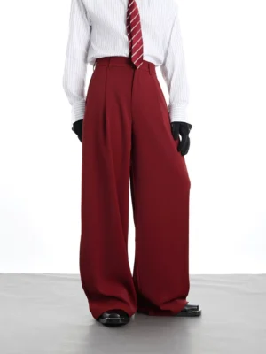 Burgundy red wide-leg tailored trousers shown from a low front three-quarter angle with sharp pleats, oversized legs, and a polished streetwear suiting silhouette