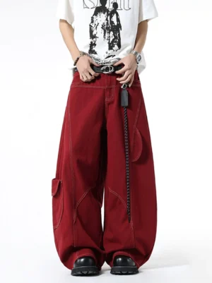 Front full-body view of oversized burgundy wide-leg cargo jeans with curved contrast stitching, utility pockets, chain leather tag, white graphic T-shirt, belt, and chunky black shoes