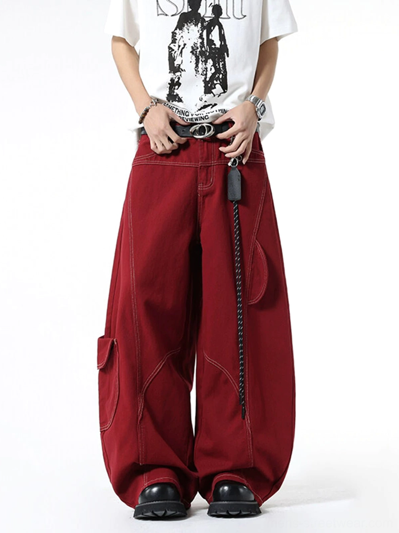 Front full-body view of oversized burgundy wide-leg cargo jeans with curved contrast stitching, utility pockets, chain leather tag, white graphic T-shirt, belt, and chunky black shoes
