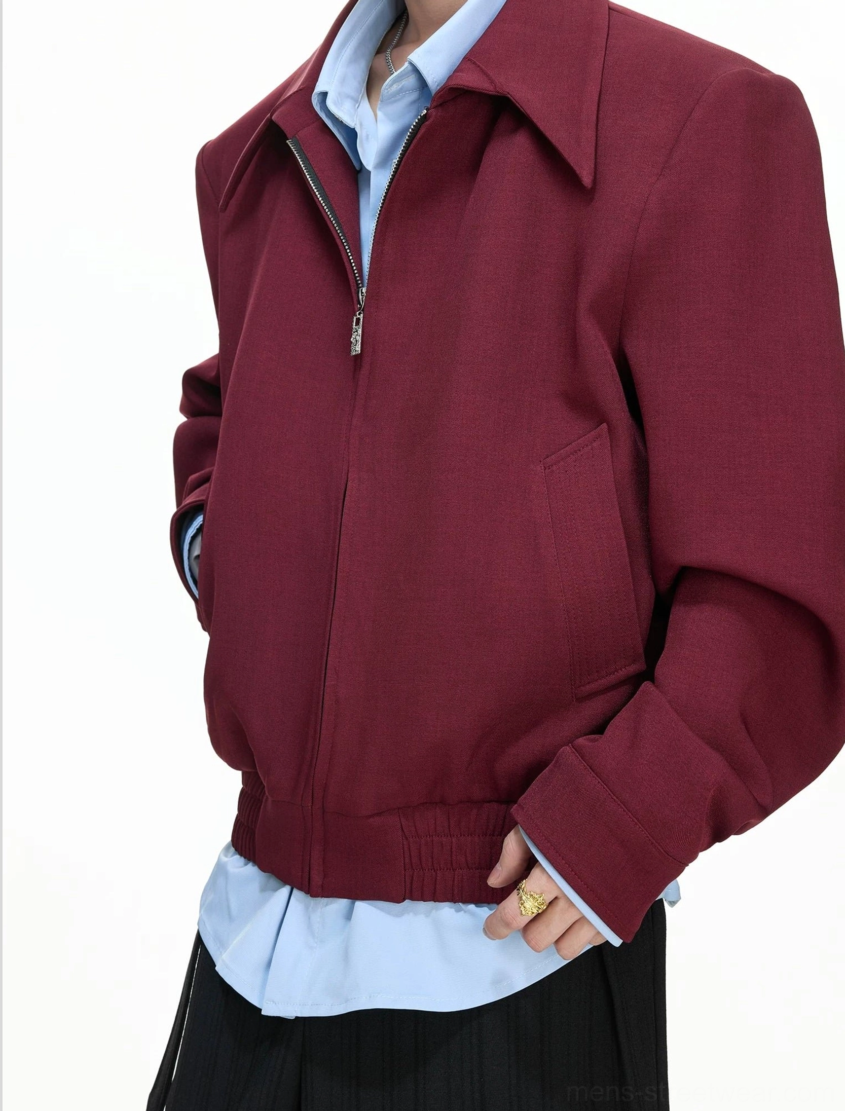Side-front view of a model wearing a burgundy zip blouson with layered shirt details and a visible side pocket