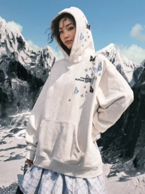 White ash butterfly embroidered oversized streetwear hoodie worn with hood up in a snowy mountain setting