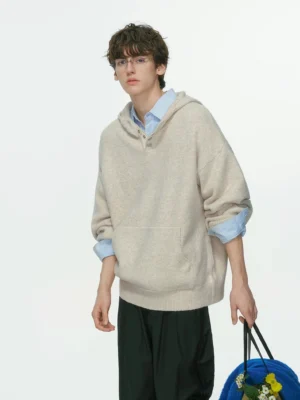 Camel apricot oversized hooded knit sweater with front kangaroo pocket layered over a collared shirt and styled with black wide-leg trousers