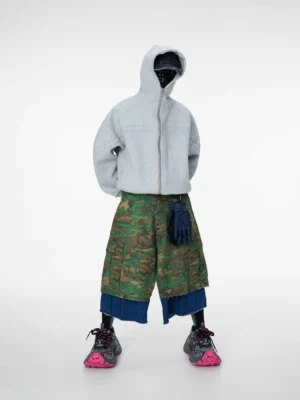 Front full view of wide-leg camouflage cargo shorts layered over frayed raw denim with utility waistband details