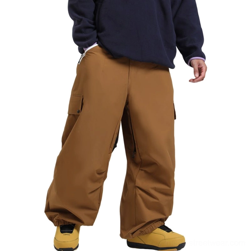Caramel brown oversized cargo snow pants with flap cargo pockets, side zipper pockets, elastic cuffs, and relaxed wide-leg ski wear silhouette