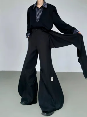 Black cascade sculpt flare trousers shown from a three-quarter front view with asymmetrical draped waist panel, ultra-wide floor-length legs, and small streetwear fabric tag