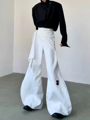 White cascade sculpt flare trousers shown from a three-quarter front view with asymmetrical wrap waist panel, dramatic wide-leg silhouette, and black thigh tag