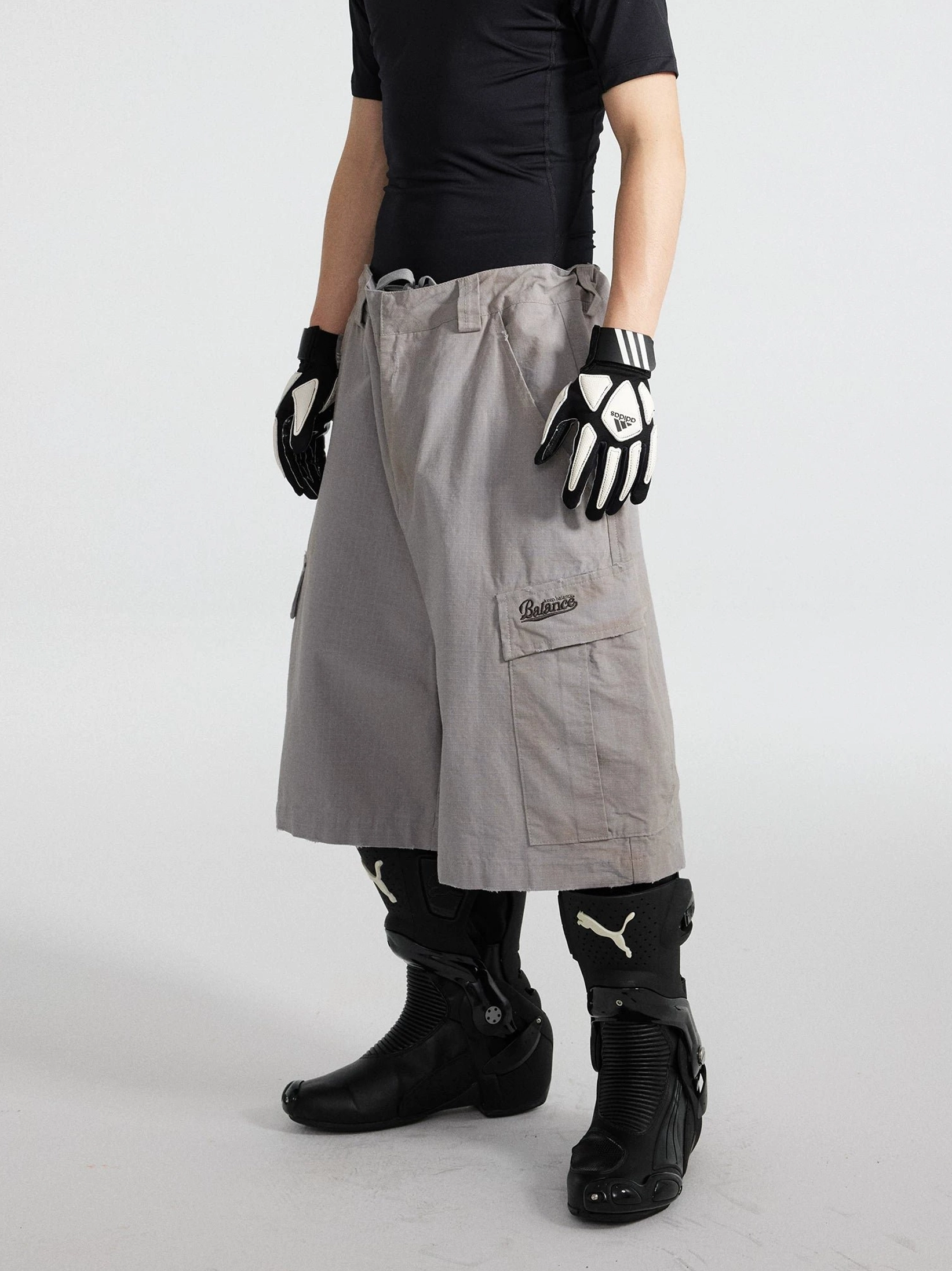 Front full-body view of cement ash wide-leg cargo culottes styled with a fitted black t-shirt, gloves, and black moto boots