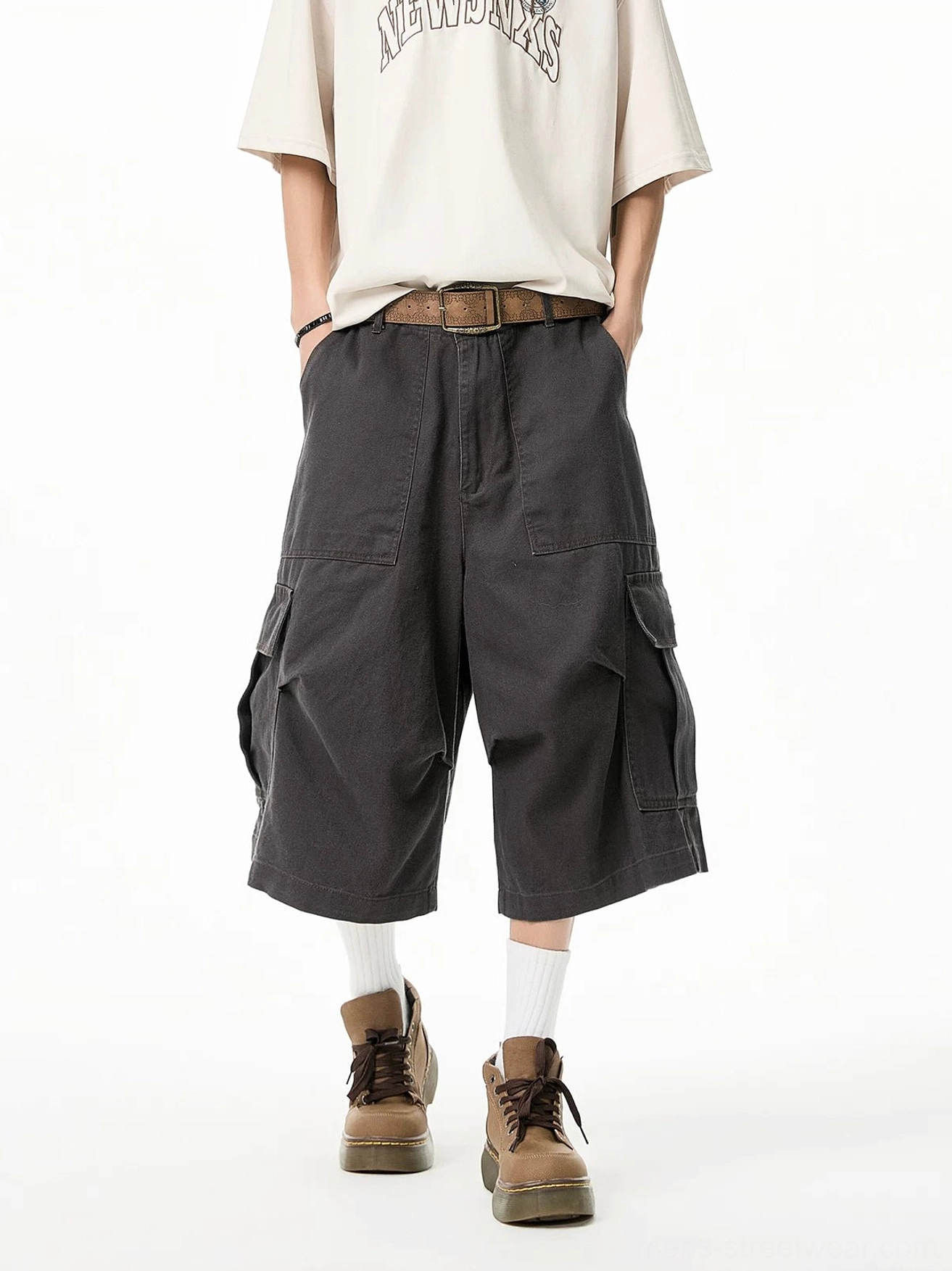 Charcoal gray baggy cargo Bermuda shorts with oversized utility pockets and long cropped length styled with a beige graphic T-shirt, white socks, and tan work boots
