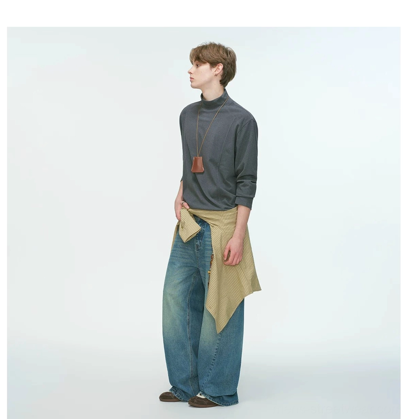 Charcoal gray men's mock neck long sleeve top paired with a leather pendant necklace and khaki shirt tied around the waist