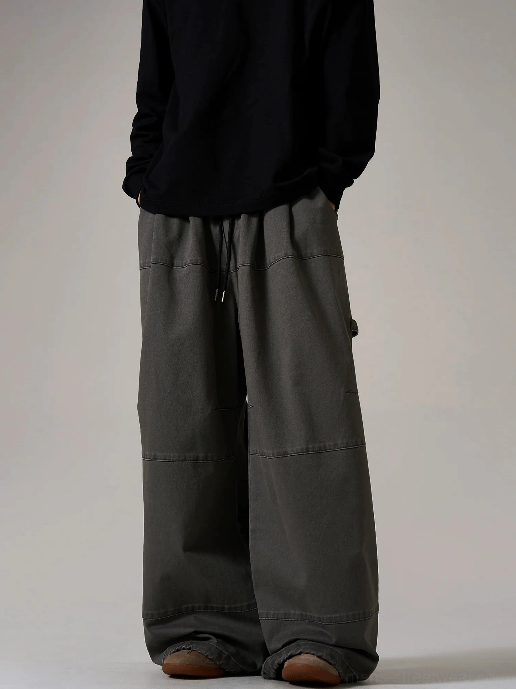 Charcoal gray oversized cargo skater pants shown from the front with wide legs, adjustable drawstring waistband, utility side detail, and streetwear panel stitching