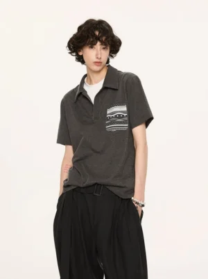 Close front three quarter view of charcoal short sleeve polo with geometric Fair Isle chest pocket and layered collar