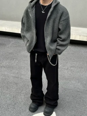 Front full-body view of a man wearing a charcoal rib-knit zip hoodie with an oversized relaxed fit in an urban concrete streetwear setting